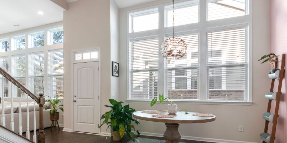 Bright modern living space with blinds, a secure entry door, high ceilings, and abundant natural light enhancing energy efficiency and comfort.