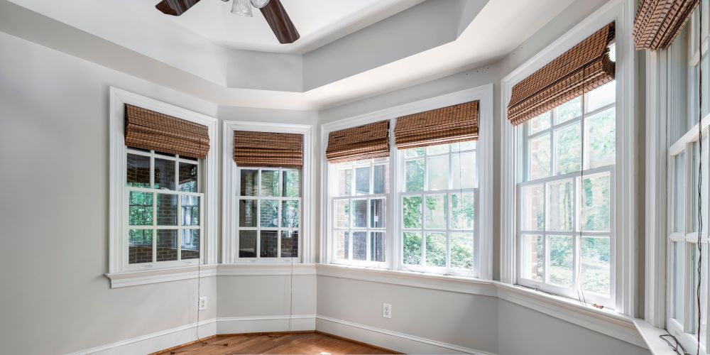 Energy-efficient in a bright bay window space with white trim, multi-pane glass, woven Roman shades, and hardwood flooring